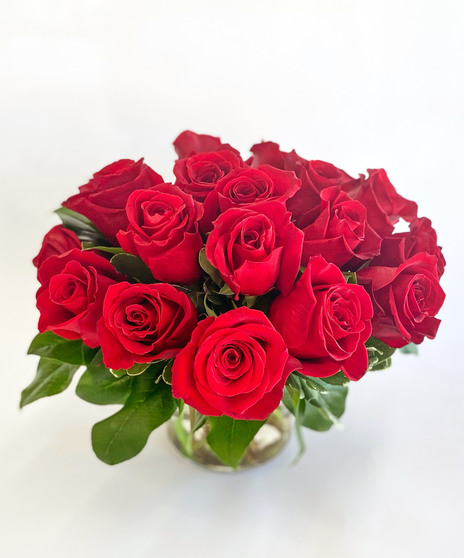Mounded roses arranged in a glass cylinder vase with lush greenery