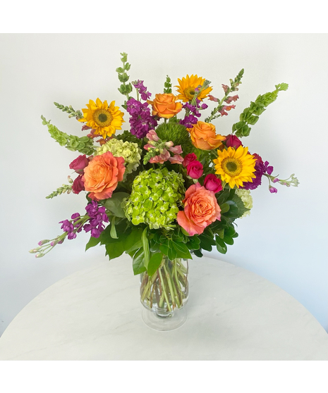 hydrangea, sunflowers, fragrant stock, and roses in a clear glass vase